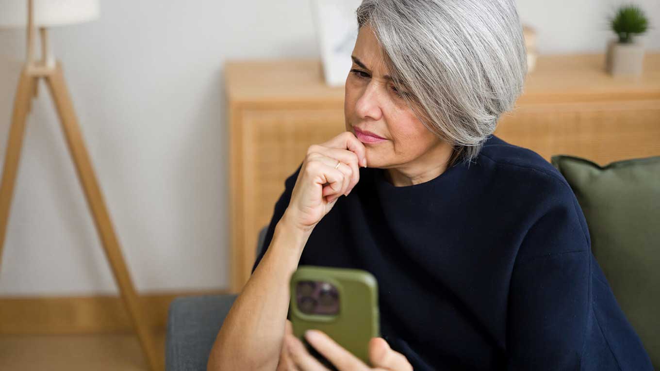 Older adult reviewing information on a smartphone while seated at home.